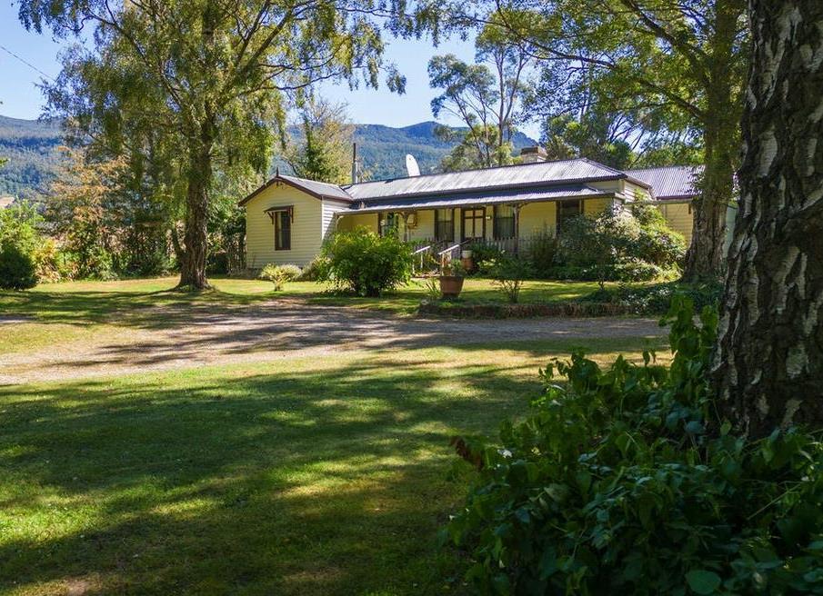 The country house at 124 Barbers Road, Meander, set among mature trees with a wide lawn and mountain backdrop